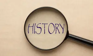 Lupa powiększająca napis "HISTORY" na papierze w kolorze beżowym.