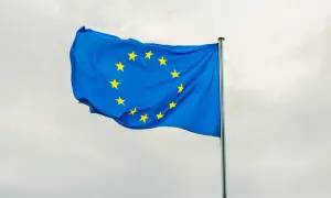 Niebieska flaga z żółtymi gwiazdami, symbolizująca europejski tytuł egzekucyjny, powiewa na maszcie na tle pochmurnego nieba.