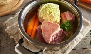 Une marmite de **potée au chou** avec des os de bœuf, des carottes, du chou et du persil, prête à mijoter.