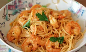 Un plat de pâtes aux crevettes, garni de persil frais, servi dans un bol décoré. Un délice pour les yeux et les papilles.