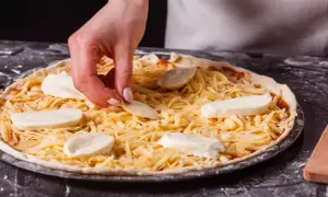 Dłoń kładzie kawałki sera na pizzy posypanej startym serem.