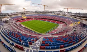 Widok na budowę nowego Camp Nou. Krany budowlane górują nad trybunami stadionu w kolorach czerwonym i niebieskim, z zieloną murawą boiska.