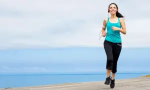 Mujer sonriente corriendo junto al mar, disfrutando de ejercicios para trabajar la autoestima y sentirse bien.