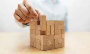 Mano che inserisce un pezzo di legno in un puzzle complesso, metafora di un efficace crisis management.
