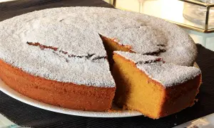 Una soffice torta carote e mandorle, cosparsa di zucchero a velo, con una fetta tagliata che ne rivela l'interno dorato.