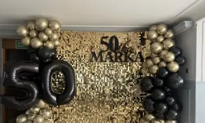 Złote i czarne balony otaczają błyszczące tło z napisem "50 lat Marka".