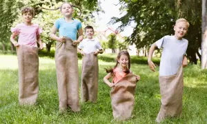 Niños compiten en carreras de sacos en un día soleado, disfrutando en familia de juegos al aire libre.