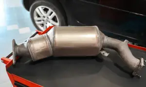 Katalizator samochodowy, kluczowy element w kontekście tego, jak jeździć dieslem, leży na stole warsztatowym obok koła pojazdu.