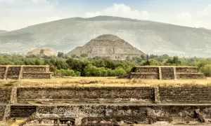 Majestätische Maya-Ruinen erheben sich vor einer sanften Bergkulisse. Alte Steinstrukturen und Pyramiden zeugen von einer vergangenen Zivilisation.
