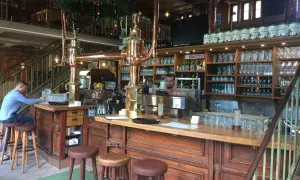 Gemütliche Atmosphäre im Brauhaus Spandau. Ein Mann sitzt am Tresen, hinter ihm Regale voller Gläser und Bierfässer.