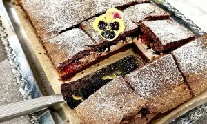 En chokladgrädde tårta skuren i bitar, pudrad med florsocker och dekorerad med violer. En tårtspade lyfter upp en bit.