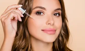 Kobieta aplikuje serum z pipetki na policzek. Dowiedz się, jak stosować retinol dla pięknej cery.