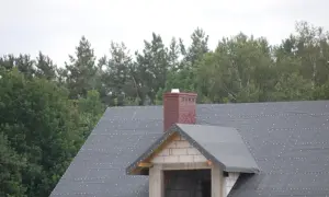 Ceglany komin na dachu w trakcie budowy. Zastanawiasz się, jak naprawić pęknięty komin? Ten obraz pokazuje jego obecny stan.