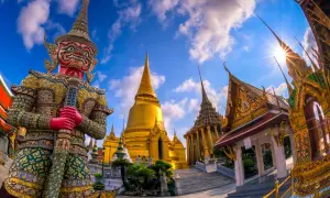 Imponerande tempel i Bangkok med en stor, färgglad jättefigur framför gyllene pagoder under en blå himmel med moln.