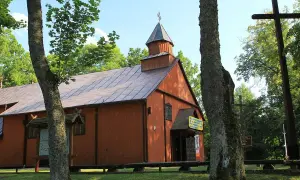 Drewniana cerkiew w Studzienicznej, jedna z lokalnych atrakcji, otoczona zielenią. Obok krzyż.