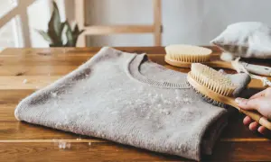 Delikatny sweter z kaszmiru z widocznymi kuleczkami, które pokazują, czy kaszmir się mechaci. Szczotka do pielęgnacji wełny w dłoni.