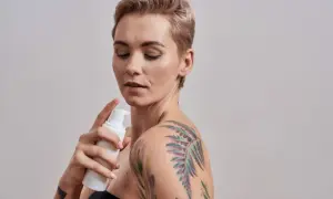 Kobieta z kolorowym tatuażem na ramieniu aplikuje piankę. Dowiedz się, czym myc tatuaz, by zachować jego piękno.