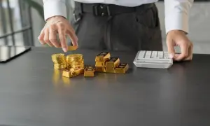 Ręce układają stosy złotych monet i sztabek, obok kalkulator. To inwestycja w złoto Heraeus.