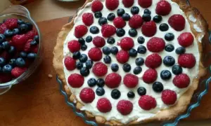 Pyszna tarta na słodko z malinami i borówkami, udekorowana kremem. Idealna na letnie popołudnie.