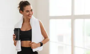 Lächelnde Frau mit Handtuch und Shaker nach dem Training. Sie fragt sich, wie viel Kreatin pro Tag für optimale Ergebnisse.