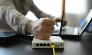 Zirytowany użytkownik próbuje dowiedzieć się, jak przyspieszyć ethernet, patrząc na router i laptopa.