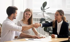 Accordo raggiunto: stretta di mano tra uomo e donna, con una collega sorridente. Si discute di stage e retribuzione minima.