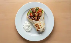 Kebab w tortilli z warzywami i sosem na białym talerzu.