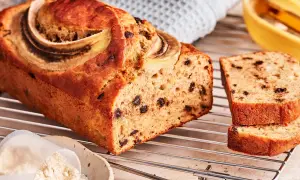Saftiges protein bananenbrot mit Schokostückchen und Bananenscheiben, daneben eine Schüssel mit Proteinpulver.