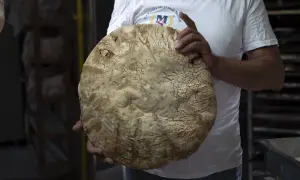 Un fornaio mostra un grande pane rustico, la cui crosta ricorda la ricetta del pane di Monte Sant'Angelo.