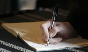 Dłoń pisze piórem w notesie. To może być moment spisywania testamentu lub umowy dożywocia, zapewniającej opiekę do końca życia.