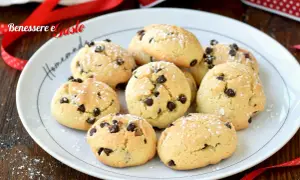 Biscotti con gocce di cioccolato spolverati di zucchero a velo su un piatto bianco, pronti per essere gustati.
