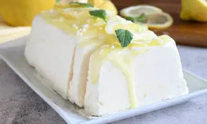 Un delizioso semifreddo al limone, guarnito con scorzette, menta e una glassa gialla, pronto per essere gustato.
