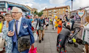 En grupp människor, inklusive Jehovas vittnen, går på en gata. En man i blå kostym leder an.