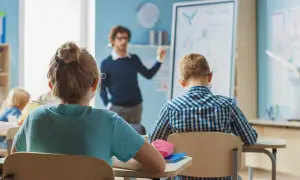 Nauczyciel tłumaczy lekcję, a uczniowie siedzą w ławkach. Czy wysokie zarobki nauczycieli wpłyną na jakość edukacji?