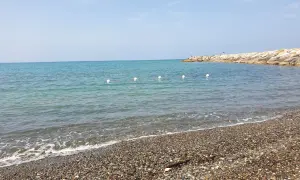 Spiagge più belle della Marina di Cecina: mare azzurro, ciottoli levigati e un molo roccioso con qualche bagnante.