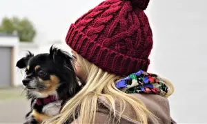 Dziewczyna w czapce w kolorze viva magenta tuli małego czarnego psa.