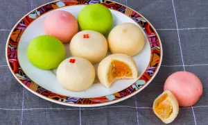 Kolorowe mochi z żółtym nadzieniem na talerzu z ozdobnym brzegiem.