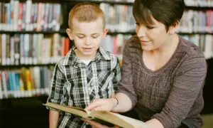 Kobieta i chłopiec czytają książkę w bibliotece. Pokazuje to, jak czytanie książek wpływa na człowieka, rozwijając wyobraźnię i wiedzę.