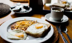 Un petit déjeuner sportif : œufs au plat, haricots et fromage râpé sur une assiette, avec une tasse de café à côté.