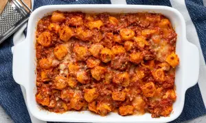 Tortelli ripieni di carne al forno, ricoperti di sugo rosso e formaggio fuso, pronti per essere gustati.