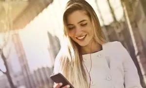 Uśmiechnięta dziewczyna słucha muzyki przez słuchawki, co oznacza słuchawka z wifi – bezprzewodową łączność ze światem.