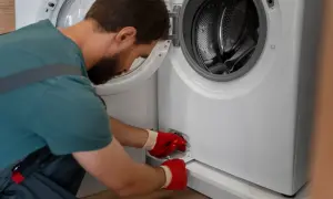 Mężczyzna w czerwonych rękawiczkach wyjmuje filtr z pralki. Dowiedz się, jak wyczyścić filtr w pralce, aby zapewnić jej prawidłowe działanie.