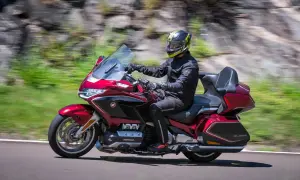 Mężczyzna w kasku jedzie czerwonym motocyklem turystycznym po drodze.