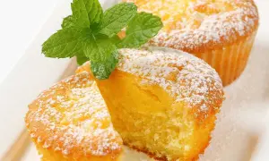 Två fluffiga citronmuffins, pudrade med florsocker och garnerade med mynta. Perfekt för ett enkelt citronmuffins recept.