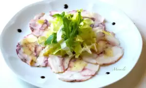 Delicato carpaccio di polpo, affettato sottile e condito con olio e limone, guarnito con insalata fresca e gocce di aceto balsamico.