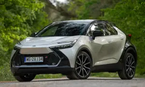 Nowy Toyota C-HR 2024 w kolorze srebrnym z czarnym dachem, zaparkowany na leśnej drodze.