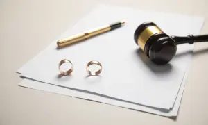 Dwa obrączki, złoty długopis i młotek sędziowski na papierze.