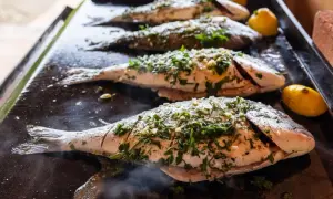 Vier Doraden werden auf einer heißen Platte gegrillt, mit Kräutern und Knoblauch gewürzt. Die Kerntemperatur der Dorade ist entscheidend für den perfekten Garpunkt.