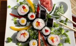 Kolorowe rolki sushi z surimi, papryką i szczypiorkiem, podane z wasabi i imbirem.