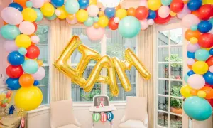Złote balony na roczek tworzą napis "LIAM" na tle kolorowej girlandy z balonów.